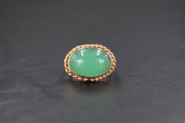 A horizontal yellow metal ring, having an oval green cabochon stone in a collared mount with twist