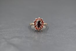 A 9ct gold red stone (possibly garnet or paste) cluster ring, the central oval cut red stone in a