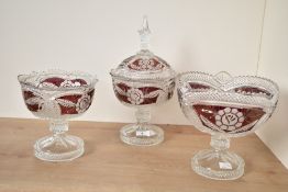 A cut glass pedestal bowl with cover, decorated with floral patterns on a cranberry colour ground,