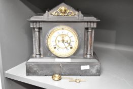 An early 20th century slate mantel clock having visible escapement, flaked either side with Doric