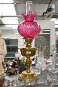 An early 20th century brass oil lamp with moulded cranberry frilled shade and glass chimney, h65cm