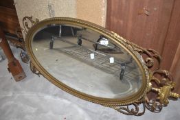An oval wall mirror having gilt frame with urn and foilate scroll decoration