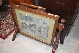 A Victorian mahogany firescreen having woolwork inset with cottage illustration, width approx. 76cm