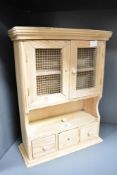 A small pine wall cabinet, having a moulded cornice over two hinged doors with metal mesh inserts