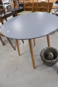 A modern circular dining table in the vintage style having grey powder coated top on beech splay