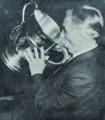 Artist unknown, black and white photograph of a man lifting a trophy to drink from it, caption - '