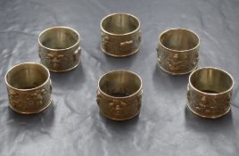 A group of six Eastern white metal napkin rings, depicting seated human figures with vacant shield