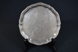 A small George V silver salver of circular form, having a moulded line and scroll rim, raised on