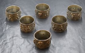 A group of six Eastern white metal napkin rings, depicting panels of human figures with vacant