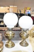 A near pair of vintage brass oil lamps, having frosted circular shade and glass chimney, raised on a