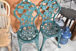 A pair of cast alloy and powder coated garden chairs, having rose themed decoration