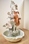 A continental style resin water figure depicting woman and cherub with urn among a flowery