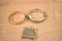 A silver hinge bangle having decorative scroll engraving, with a gold plated hinge bangle also