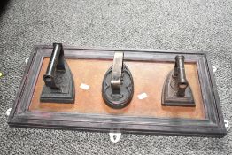 Three antique irons mounted to a wooden board, L59cm