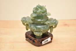 A Chinese green stone lidded censor with Foo dog mask handles supported on a carved wooden stand,