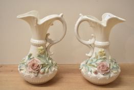 A pair of Belleek porcelain jugs having shaped handle and spout, decorated with floral patterns