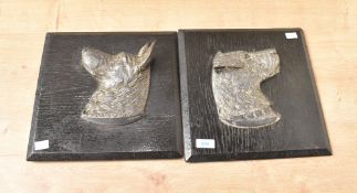 A pair of Continental cast silver-plate dog head plaques, mounted to black stained and chamfered oak