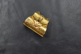 A yellow metal presumed gold handbag trinket locket, having scroll engraving and buckle decoration