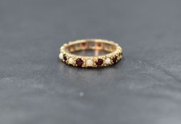 A 9ct gold garnet and pearl set full eternity ring, the alternating round cut garnets and split