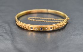 A Victorian 9ct gold hinged bangle having three inset sapphires interspersed by two small diamonds