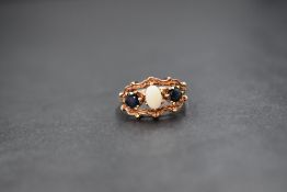 A 9ct gold opal and sapphire ring, the central opal flanked by two sapphires in an open moulded