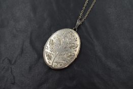 A silver locket and chain, the oval silver locket having decorative floral engraving to the front,