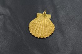 A yellow metal shell motif pendant, having a textured finish, marked 18ct, 3.5cm including loop, 6g