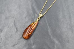 A yellow metal set amber pendant, the freeform amber on an articulated yellow metal pendant loop
