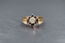 A 9ct gold diamond and sapphire set cluster ring, the raised central illusion set diamond chip in an