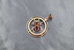 A yellow metal insect pendant having a central garnet set spider in a circular surround, bearing