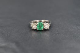 An early 20th century white metal emerald and diamond three stone ring, having a central baguette