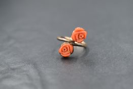 A yellow metal presumed gold coral set ring, the two rose motif carved coral in a cross over