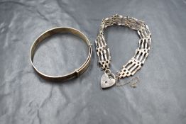 A silver four bar gate bracelet, having a silver heart padlock and broken safety chain, along with a