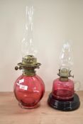 A 19th century oil lamp having cranberry glass body and clear glass chimney raised on a footed base,