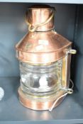 An early 20th century copper ships lantern converted into a lamp, having shaped brass handle,