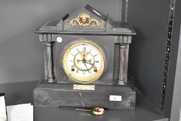 An early 20th century slate mantel clock having visible escapement, flaked either side with Doric