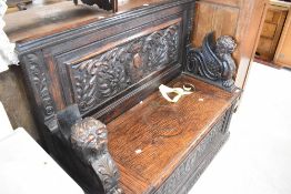 A traditional monks style bench having fixed back and winged lion creature handles , heavily