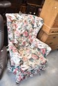 An early 20th Century wingback armchair on Queen Anne revival style legs and having loose covers