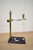 A brass and cast-metal adjustable candle stand, the brass arm with three pivoting sections adjusting
