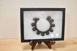 An African currency bracelet decorated with geometrical designs, held behind a glass frame for