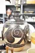 A large black-glazed pottery lamp having a rounded body and narrow neck, measuring 53cm tall, no