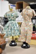 A pair of miniature manikins styling two vintage dresses, measuring 52cm respectively.