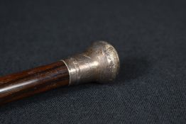 A white metal mounted walking stick, the pommel having rubbed scroll decoration and monogram to top,