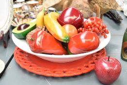 A decorative display of wooden, stone and synthetic fruit, within a white ceramic bowl with red