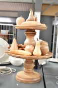 A wooden two tier cake stand, h38cm, sold together with a quantity of wooden fruit