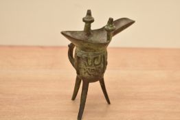 A Chinese metal ritual vessel on tri pod legs, having shaped spout and handle, h16cm