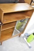 A vintage teak laminate bookcase having one open shelf and two behind sliding glass doors, width