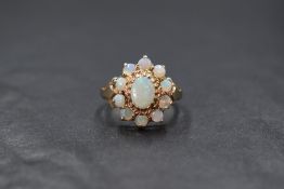 A 9ct gold and opal cabochon open cluster ring having a central oval opal within a surround of ten
