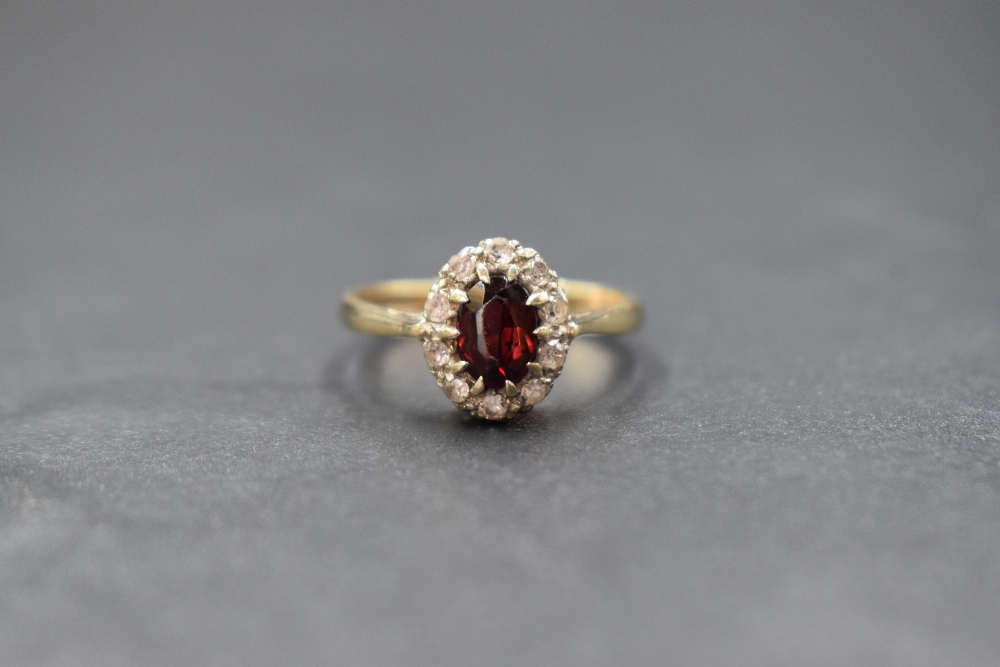 A 9ct gold garnet and white gemstone set cluster ring, the central oval cut garnet in a ten white
