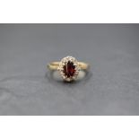 A 9ct gold garnet and white gemstone set cluster ring, the central oval cut garnet in a ten white